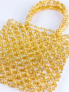 Détail d'un sac à main tissé main avec perles acryliques dorées et structure grille
