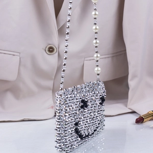 Handmade silver beaded crossbody bag with smiley face and pearl strap on beige blazer background