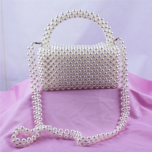 Sac à main artisanal en perles blanches avec bandoulière sur fond en satin rose