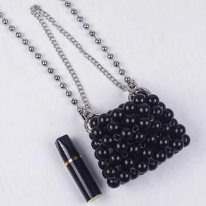Close-up of a handmade black beaded mini bag with silver chains and a lipstick for scale