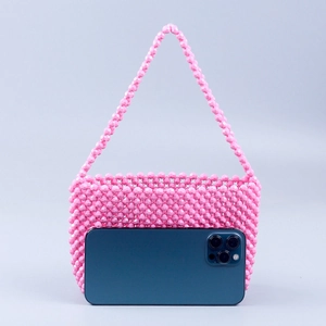 Pink acrylic beaded handmade shoulder bag with woven finish next to a smartphone for scale