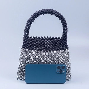 Mini sac à main en perles noires mates et argentées à côté d'un smartphone