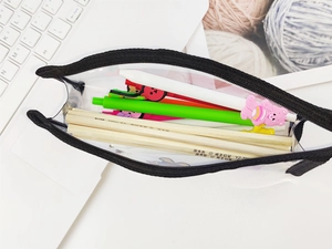 Vue de dessus d'une trousse transparente en PVC ouverte avec fermeture éclair noire et stylos