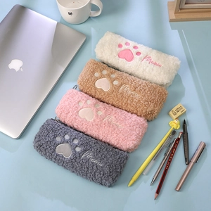 Fuzzy plush cat paw pencil cases in four colors on a desk with stationery items