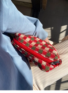 Gedetailleerde textuur van de rood-groen geruite gebreide tas met metalen ritssluiting