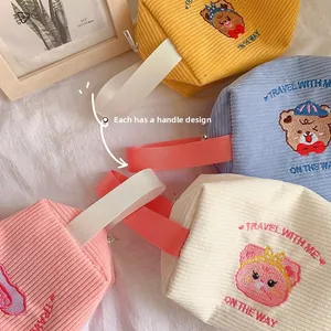 Detail of embroidered corduroy makeup bags in pastel colors with a soft fabric handle
