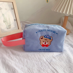 Detail of cute bear embroidery and travel text on textured blue corduroy makeup bag
