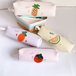 Dettaglio di ricami di frutta e trama a quadri su astucci in tela color caramello