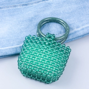 Detailed close-up of green acrylic beaded handbag with round handles on denim background