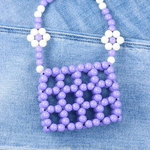 Detail of handmade purple beaded mini bag featuring white flower accents on denim background