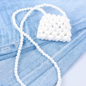Detail of hand-woven white faux pearl mini crossbody bag on blue denim background
