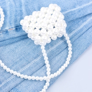 Detailed close-up of a handmade white pearl beaded mini bag on denim background