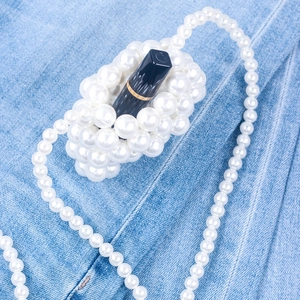 Detail of handmade beaded white pearl lipstick bag with long chain on denim background