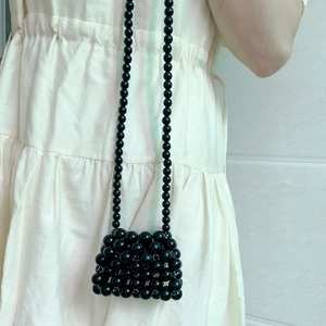 Detail of a handmade black beaded mini bag with glossy finish and long thin crossbody strap