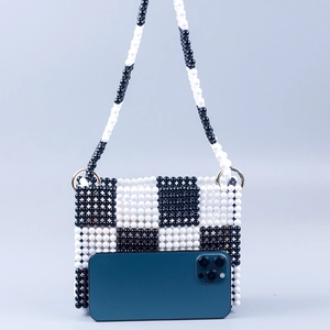 Detailed view of handmade black and white checkered beaded bag with phone for size reference