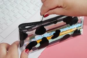 Close-up of hands opening a transparent PVC pencil case with black heart patterns