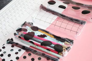 Detail of transparent PVC pencil cases with grid and dot patterns on a pink desk