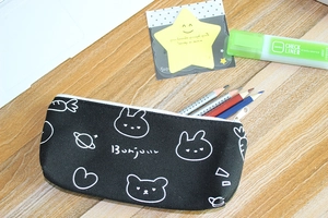 Close-up of black canvas pencil case with cute rabbit and planet motifs on wooden desk