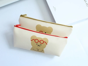 Close-up of two beige cartoon bear pencil cases with smooth PU leather texture and zippers
