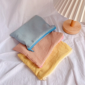 Three assorted plaid and striped cotton zipper pouches stacked by a warm bedside lamp