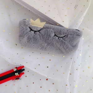 Close-up of grey plush pencil case with eyelash embroidery and a gold sequin crown