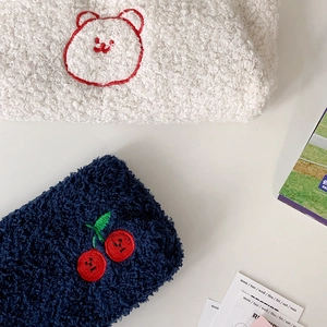 Detail of plush stationery pouch featuring cherry and bear embroidery in soft fleece material