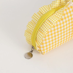 Detail of yellow checkered pencil case featuring delicate ruffle trim and metal zipper