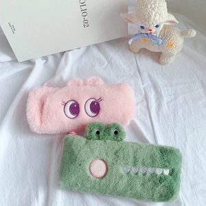 Close-up of soft plush pencil cases with cute embroidered eyes and green crocodile design