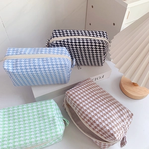 Flat lay of houndstooth cosmetic bags in four colors on a minimal desk setup