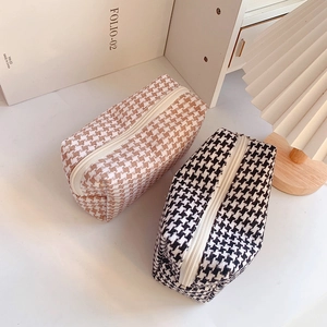 Detailed view of two houndstooth cosmetic bags in brown and black with top zippers