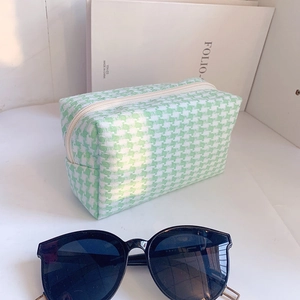 Detail of green and white houndstooth pouch with zipper closure and sunglasses