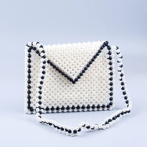 Detail of handcrafted cream pearl envelope bag with black bead trim and strap