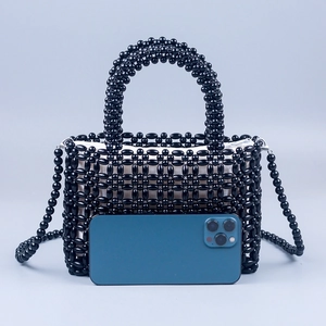 Borsa a mano in perline nere con manico e tracolla accanto a uno smartphone per le dimensioni