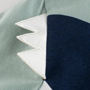 Détail d'un t-shirt en coton vert menthe avec applique de dinosaure marine et broderie blanche