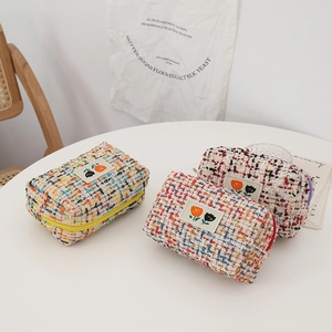 Detail of tweed makeup bags with tulip embroidery and gold zipper in three soft colors
