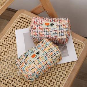Tweed makeup bags with embroidered tulip labels on a vintage woven chair background