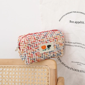 Tweed makeup bag with floral embroidery and gold thread on a vintage wooden chair