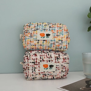 Detail of tweed makeup bags featuring floral patches and woven texture in two colors