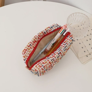 Detail view of colorful tweed makeup pouch with red zipper and various stationery inside