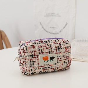 Detail of multi-color tweed makeup bag featuring purple zipper and floral patch
