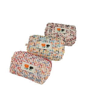 Three colorful tweed makeup bags with floral patches displayed in a row on white background