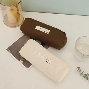 Detail of minimalist canvas pencil cases in brown and cream with ruler tag on white desk