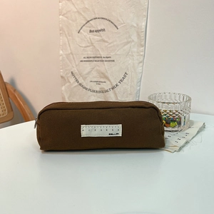 Detail of a brown canvas pencil case featuring a white woven scale label and zip closure
