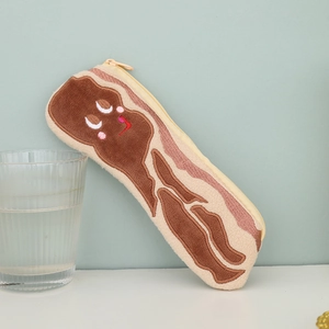 Cute bacon shaped plush pencil case with embroidered expression leaning on a glass cup