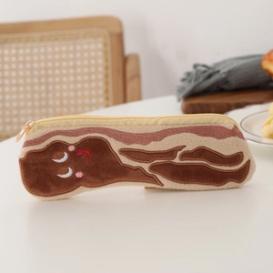 Detail shot of the plush bacon pencil case with cute embroidery on a minimal white desk