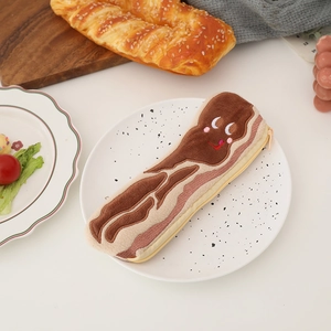 Detailed view of plush bacon pencil case with cute embroidery placed on a white ceramic plate