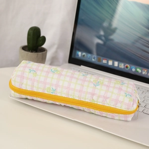 Detailed close-up of quilted floral plaid pencil case with yellow zipper on desk
