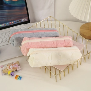 Close-up of quilted plush pencil cases in cream white, pink, and grey with metal zippers