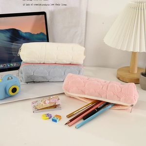 Three plush quilted pencil cases in cream, grey, and pink set on a cozy desk display