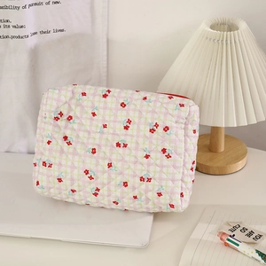 Quilted floral makeup bag with red zipper and green plaid pattern on a white desk